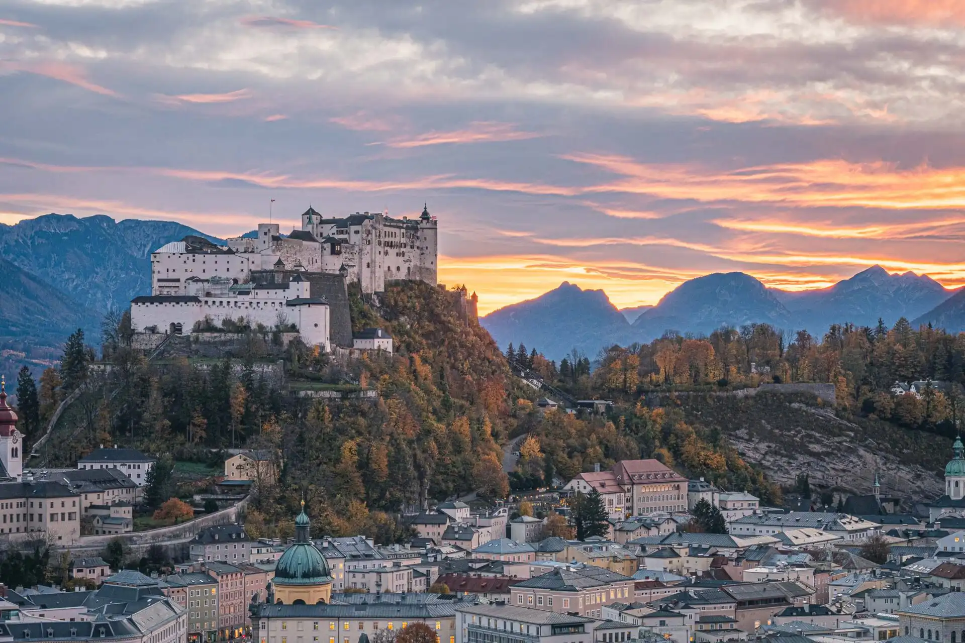 hohensalzburg fortress glowing at sunset with alpine peaks behind in salzburg.