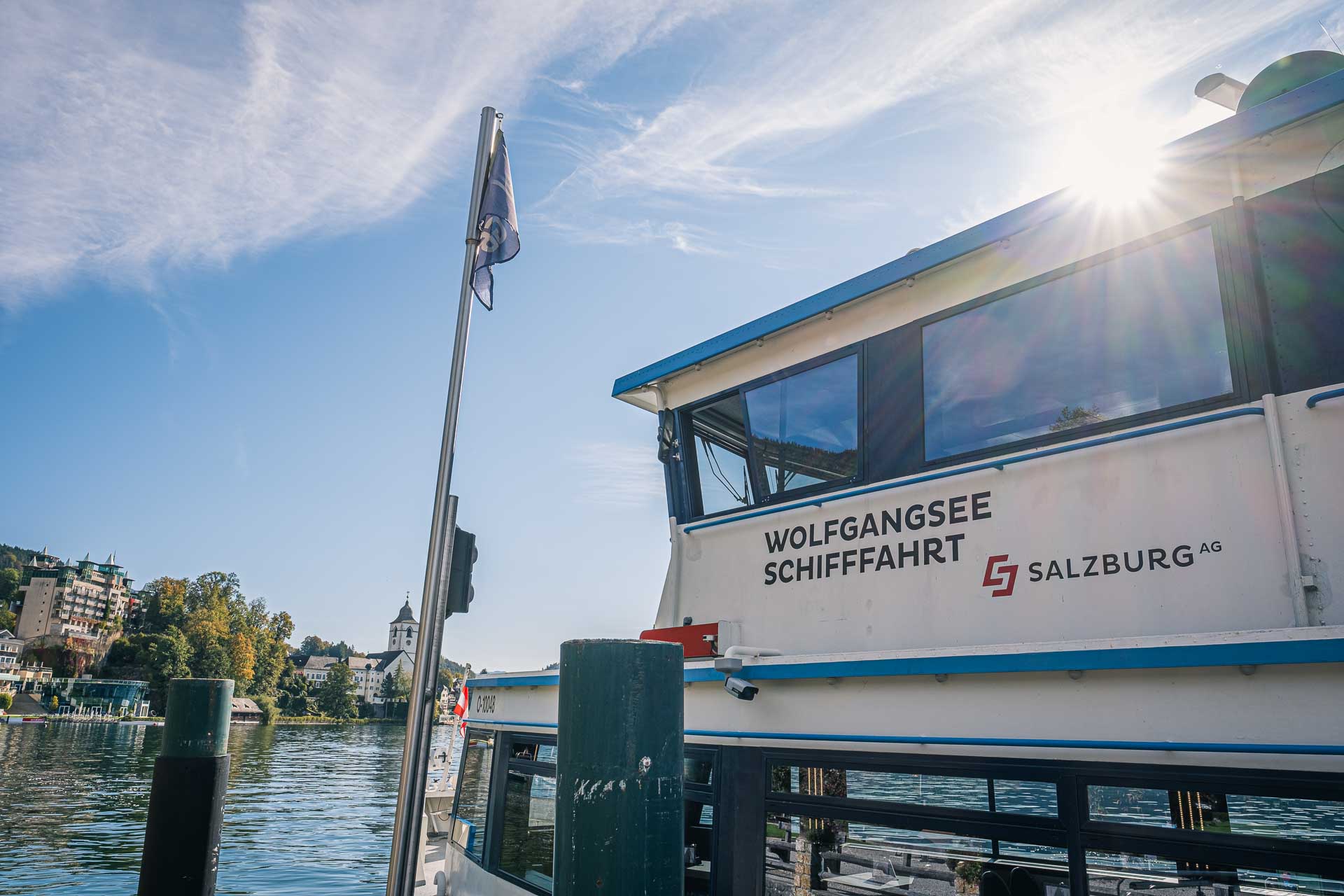 Passenger boat docked at the wolfgangsee lake under a clear blue sky with the sun shining.