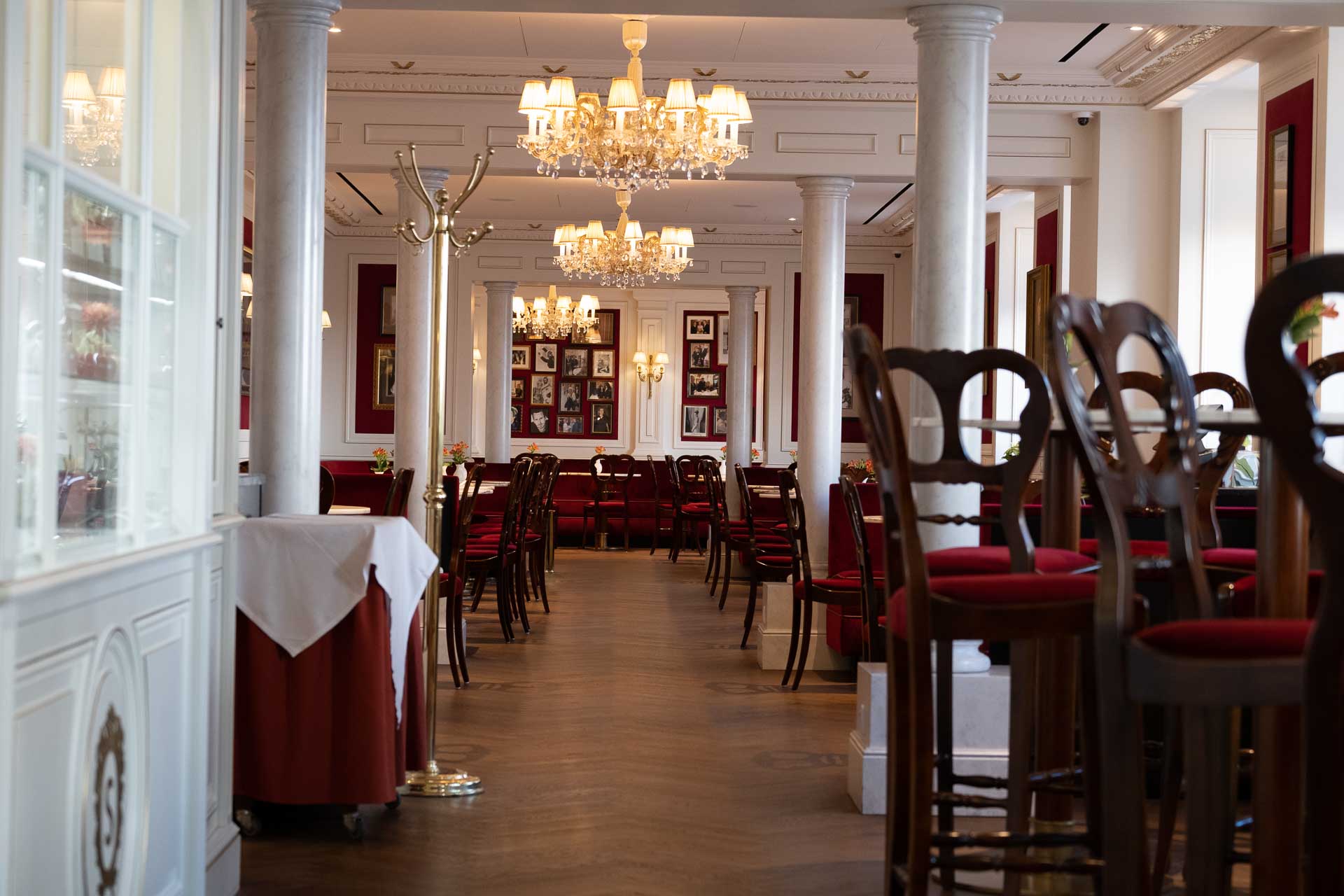 Elegant dining room with red chairs, white linen-covered tables, and chandeliers.