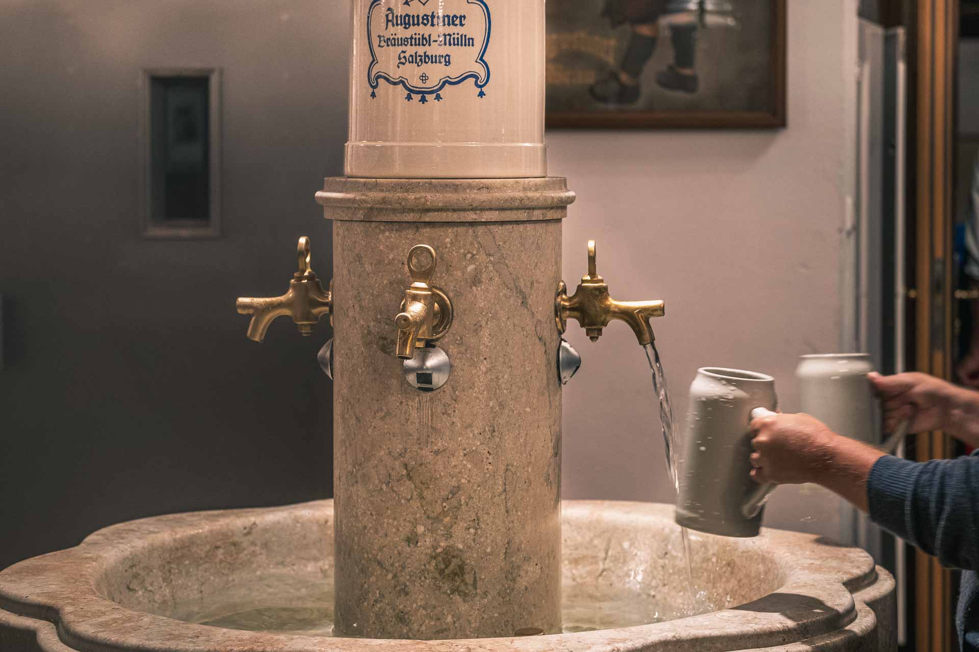 A person filling a mug from a traditional water fountain with multiple taps.